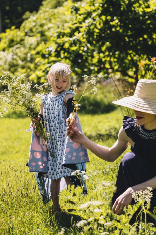Young girl in a handmade hand-smocked summer dress with Jaipur block print fabric, holding wildflowers in a sunlit meadow – ethically made children’s clothing by Darling You.